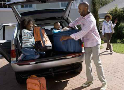 Son and daughter (6-10) helping father load luggage in back of c